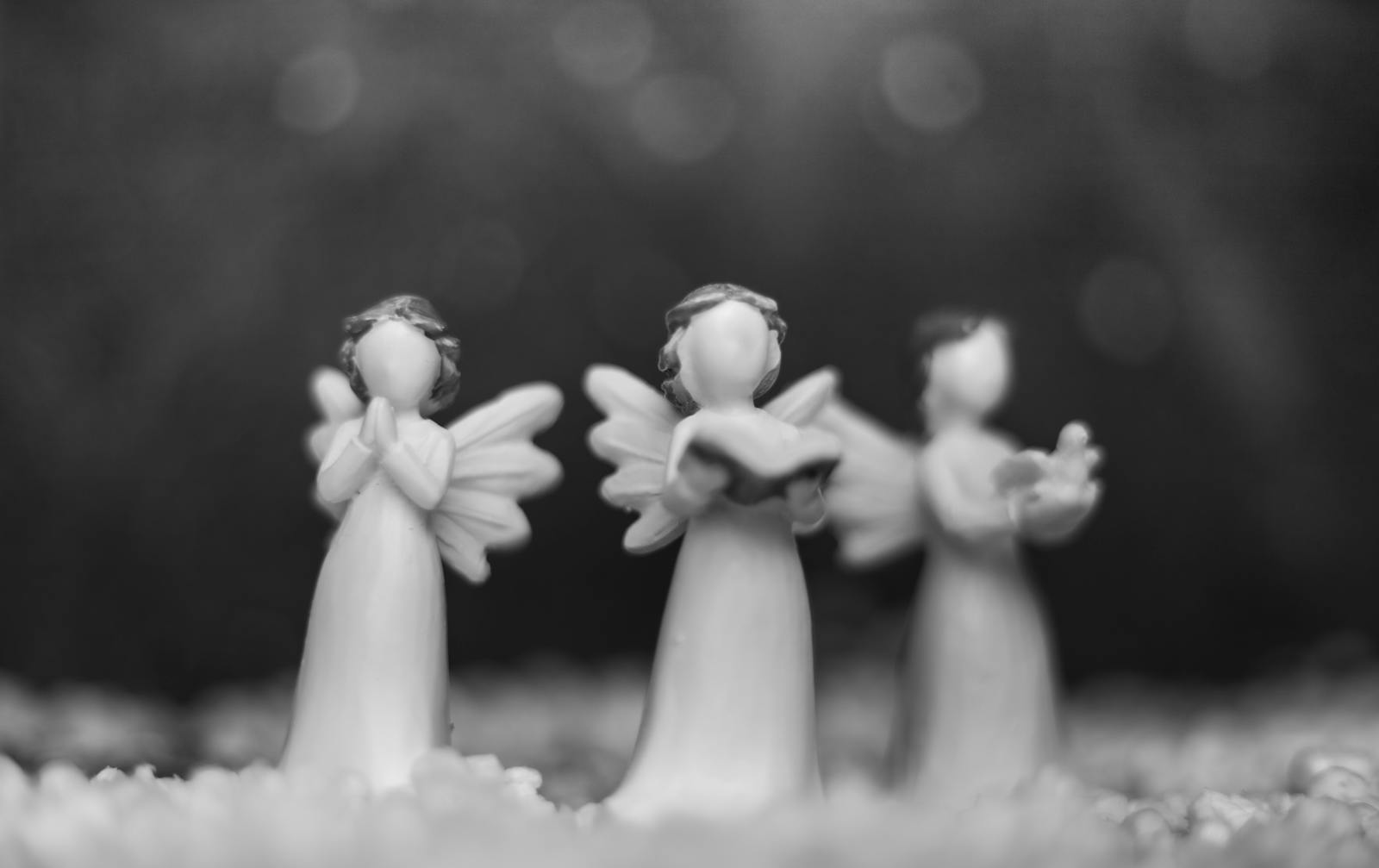 Black and white close-up of angel figurines with a blurred background, creating a peaceful mood.